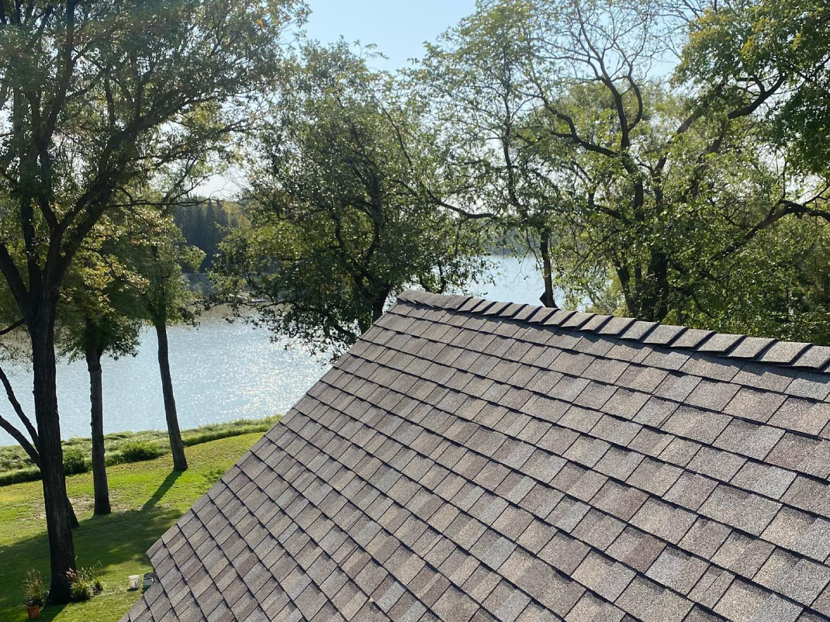 A close-up of a shingled roof with a view of a serene lake and lush trees in the background.