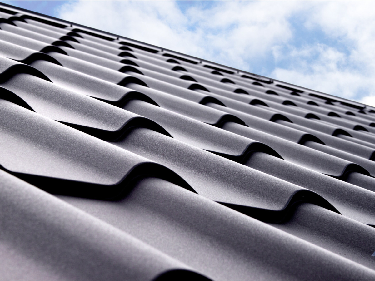 A low-angle shot of gray wavy roof tiles against a blue sky with clouds.